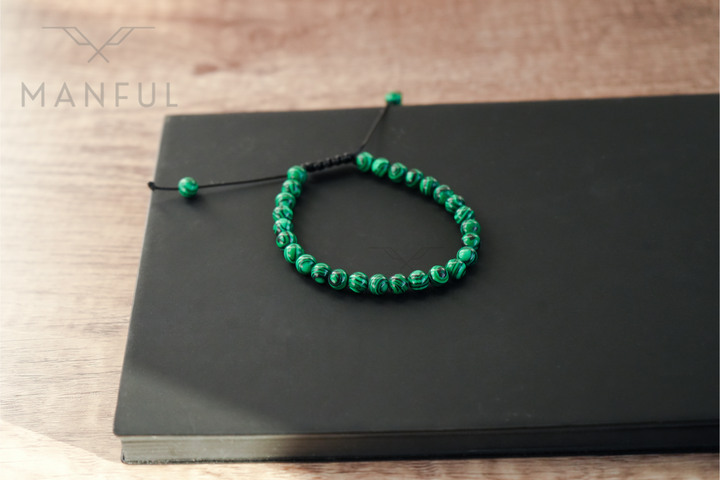Malachite Bead Bracelet, laid in a loop on a dark book with its adjustable cord ends visible