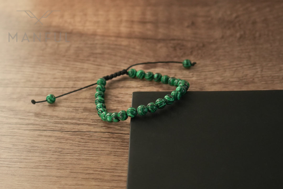 Malachite Bead Bracelet, draped over the edge of a dark surface with the cord hanging loose