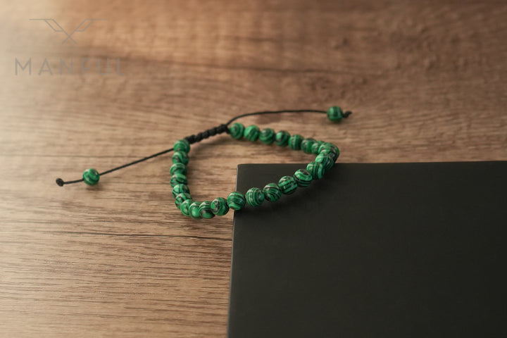 Malachite Bead Bracelet, draped over the edge of a dark surface with the cord hanging loose