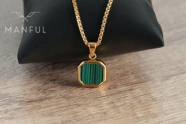 Malachite Square Necklace Gold, leaning against a black pouch on a wood surface
