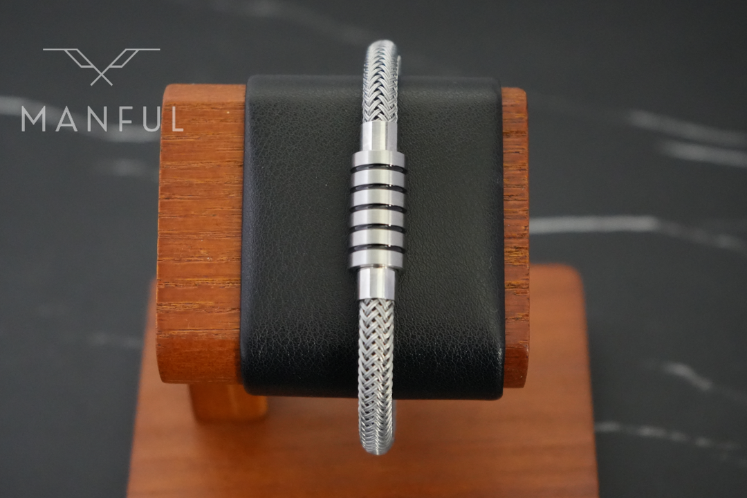 Steel Wire Bracelet Silver, displayed upright on a wooden stand with a black leather cushion