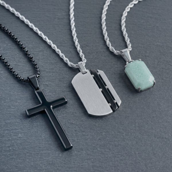 Mens Chains Collection, a black cross, a silver dog tag and a jade pendant on chains laid on dark slate