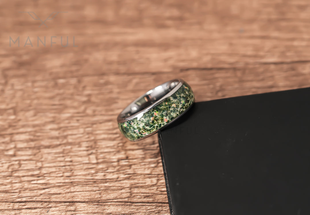 Moss Agate & Crushed Opal Ring, leaning against a black block on a wood surface