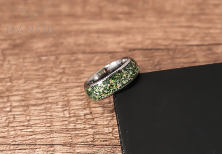 Moss Agate & Crushed Opal Ring, leaning against a black block on a wood surface