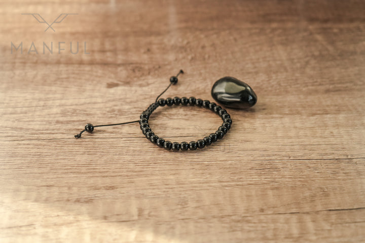 Onyx Bead Bracelet, laid on wood beside a polished onyx stone
