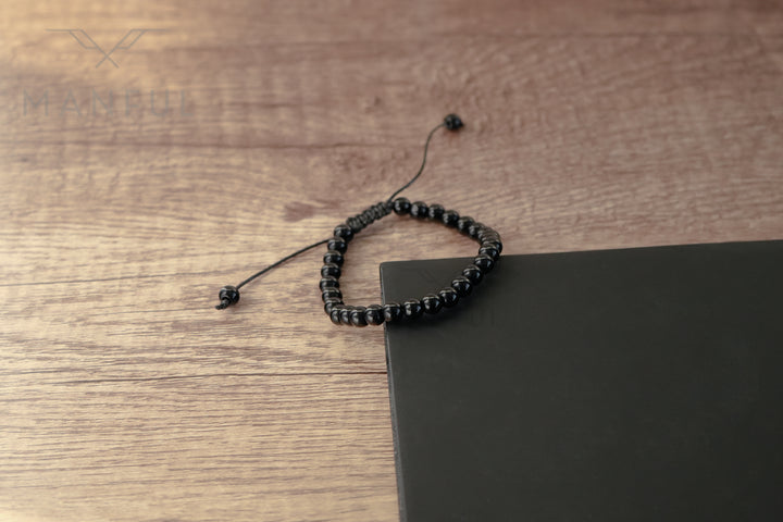 Onyx Bead Bracelet, draped over the corner of a dark notebook on wood