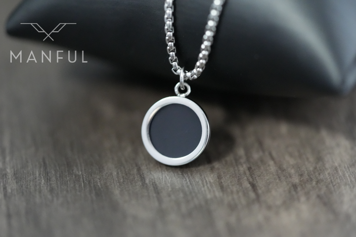 Onyx Circle Necklace, resting against a black leather cushion on a wood surface