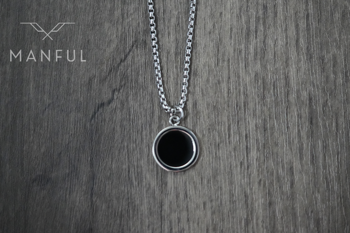 Onyx Circle Necklace, hanging against a wood surface facing the camera