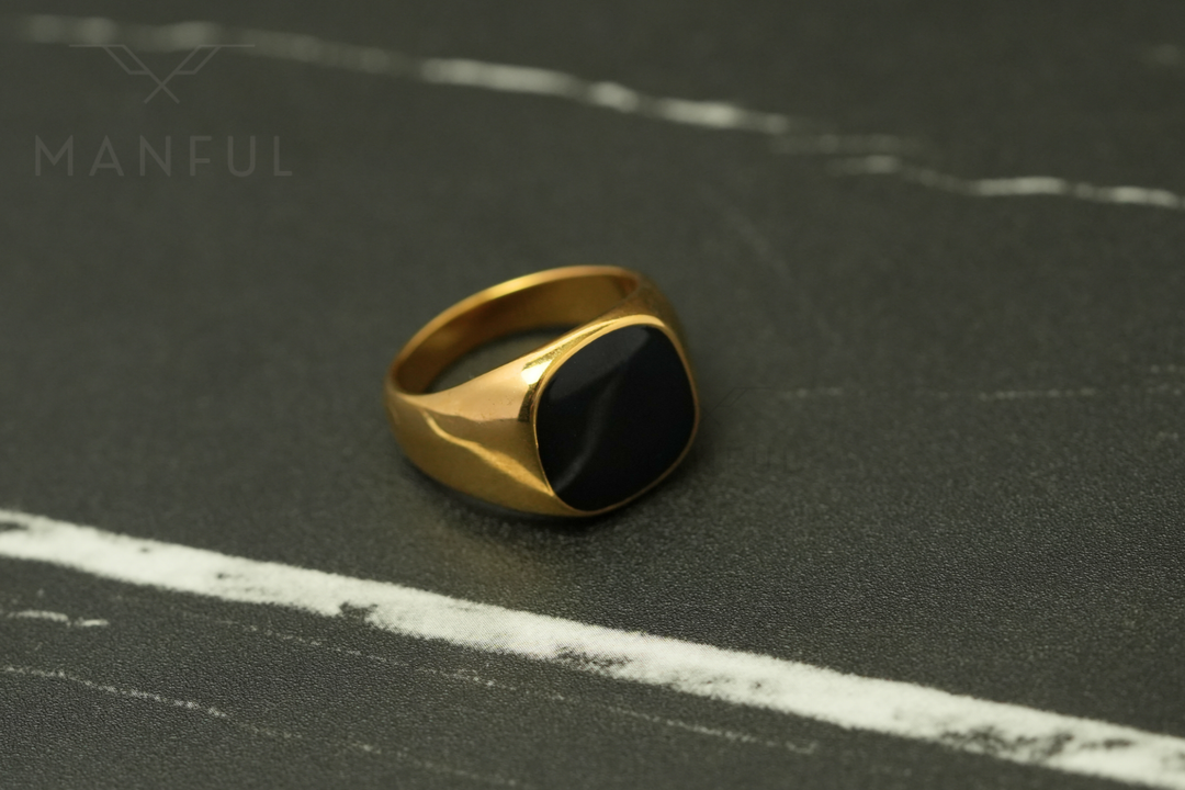 Onyx Signet Ring Gold, angled on a dark marble surface with white veining