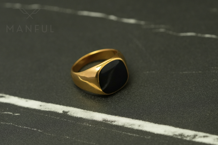 Onyx Signet Ring Gold, angled on a dark marble surface with white veining