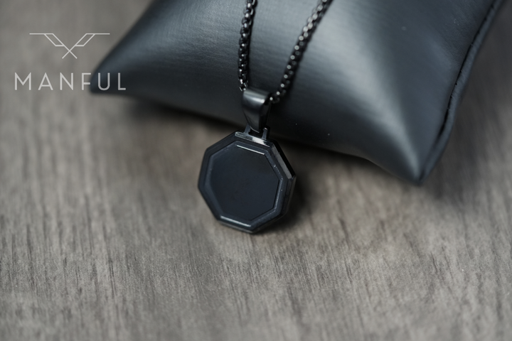 Onyx Octagon Necklace Black, draped over a dark leather cushion prop on wood
