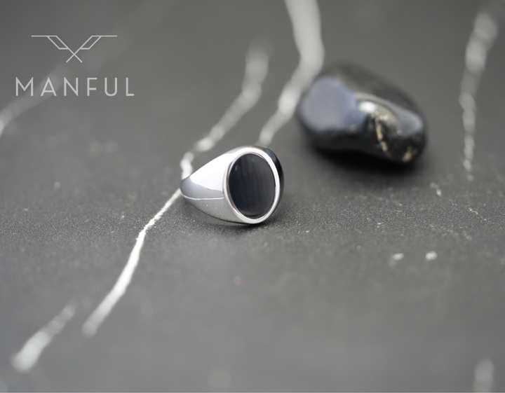 Onyx Oval Signet Ring, standing on a dark marble surface beside a polished black stone