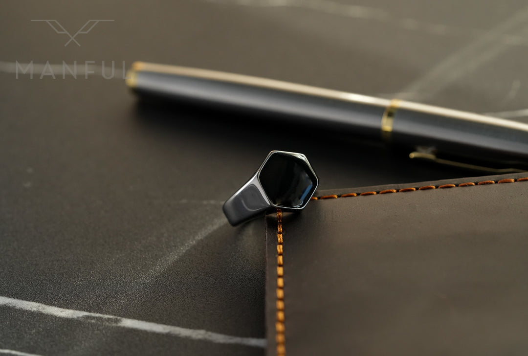 Onyx Silver Hexagon Signet Ring, propped against a stitched leather notebook edge with a pen behind
