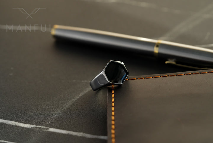 Onyx Silver Hexagon Signet Ring, propped against a stitched leather notebook edge with a pen behind