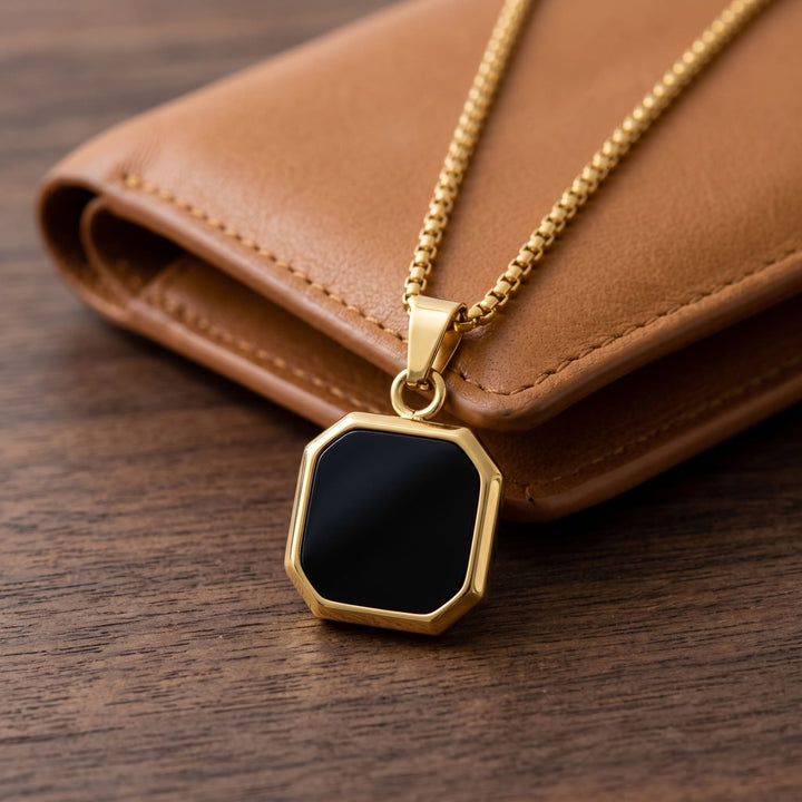 Onyx Square Necklace (Gold) draped over a tan leather wallet on a walnut desk