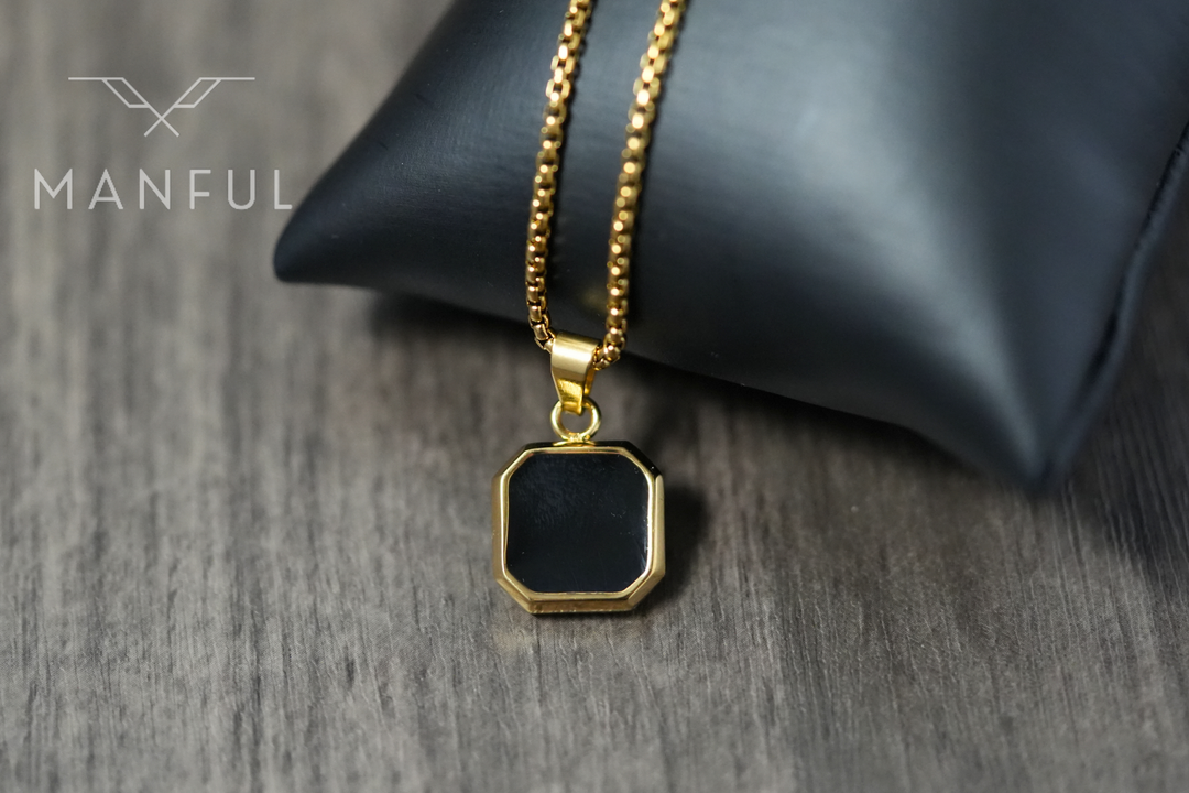 Onyx Square Necklace Gold, resting against a black leather cushion on a wood surface