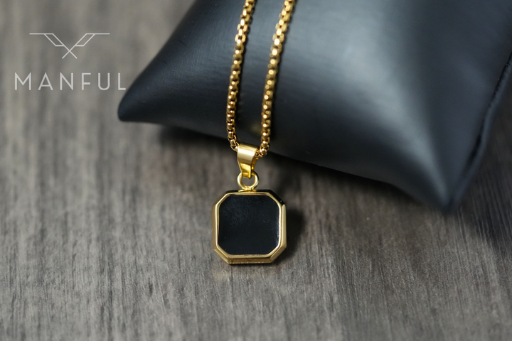 Onyx Square Necklace Gold, resting against a black leather cushion on a wood surface