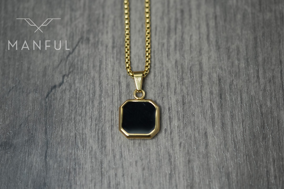 Onyx Square Necklace Gold, hanging against a wood surface facing the camera