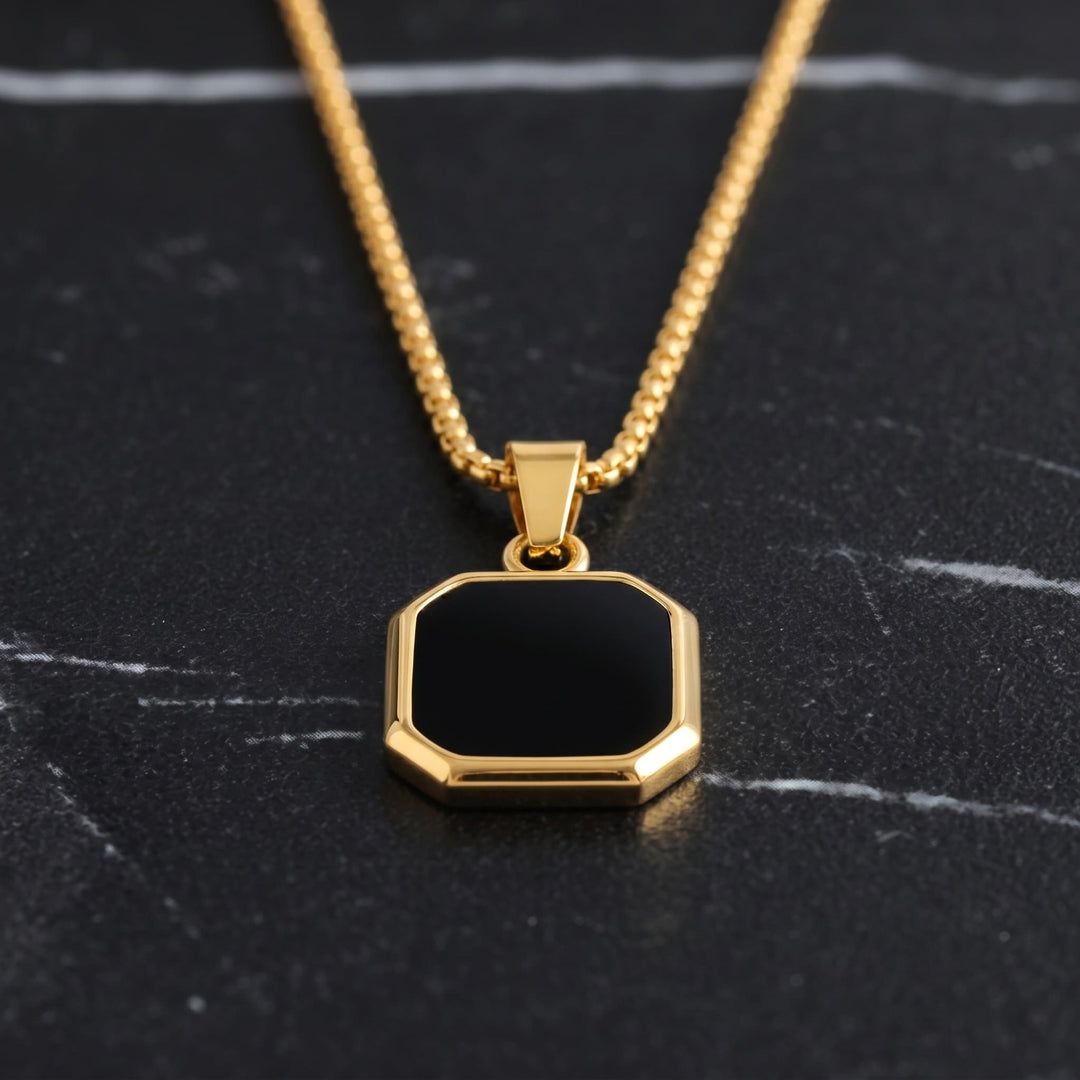 Onyx Square Necklace (Gold) lying on dark marble with the gold chain leading up