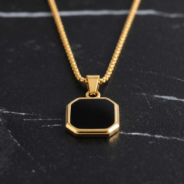 Onyx Square Necklace (Gold) lying on dark marble with the gold chain leading up