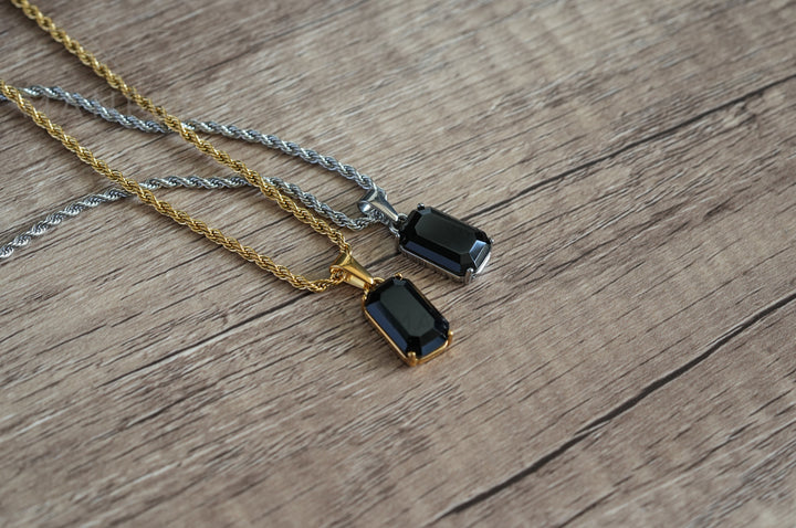 Onyx Stone Pendant Gold, shown on wood beside a matching pendant on a silver chain
