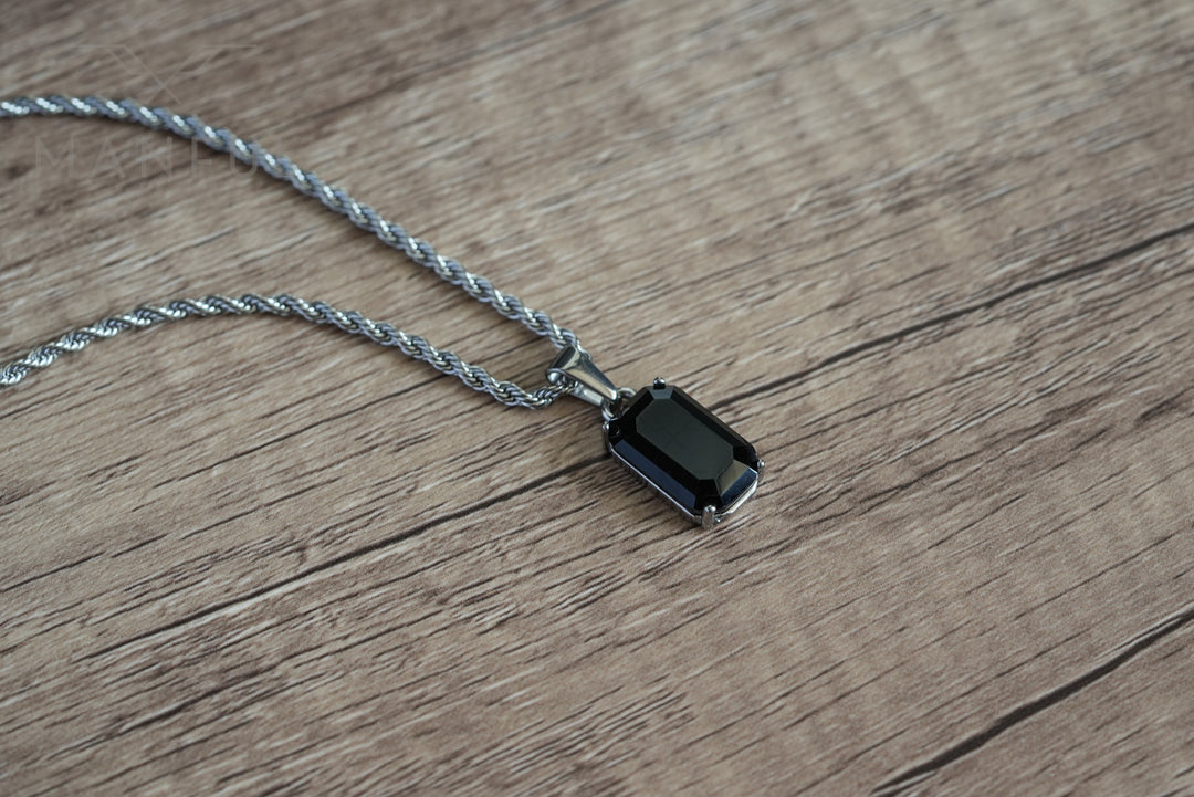 Onyx Stone Pendant Silver, lying on a wood surface with the chain draped loosely above it
