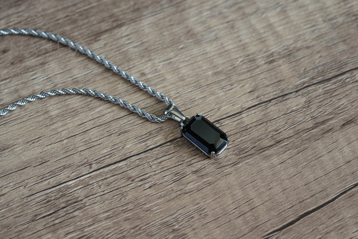 Onyx Stone Pendant Silver, lying on a wood surface with the chain draped loosely above it