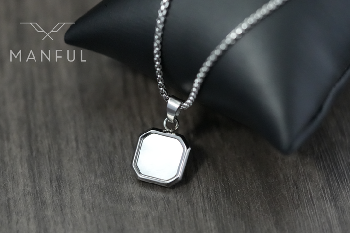Pearl Square Necklace, pendant leaning against a black leather cushion on a wood table