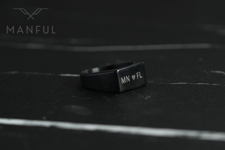 Rectangular Signet Ring Black, lying on dark marble showing custom engraved initials on the face