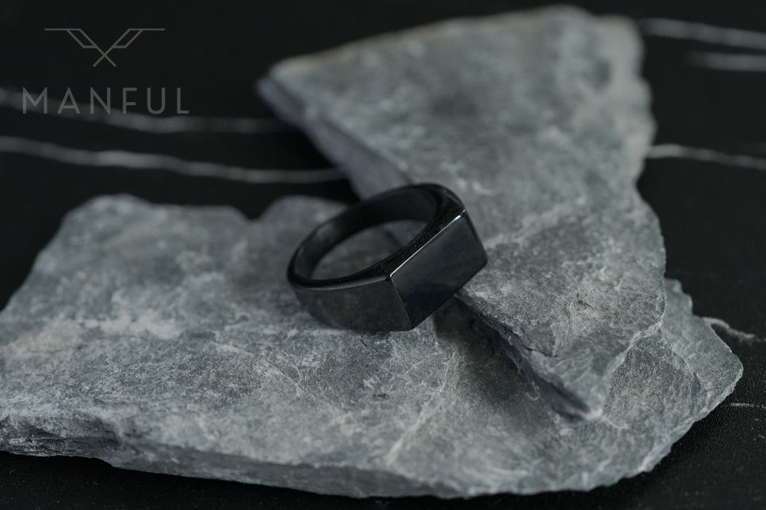 Rectangular Signet Ring Black, resting on a grey stone slab against a dark background