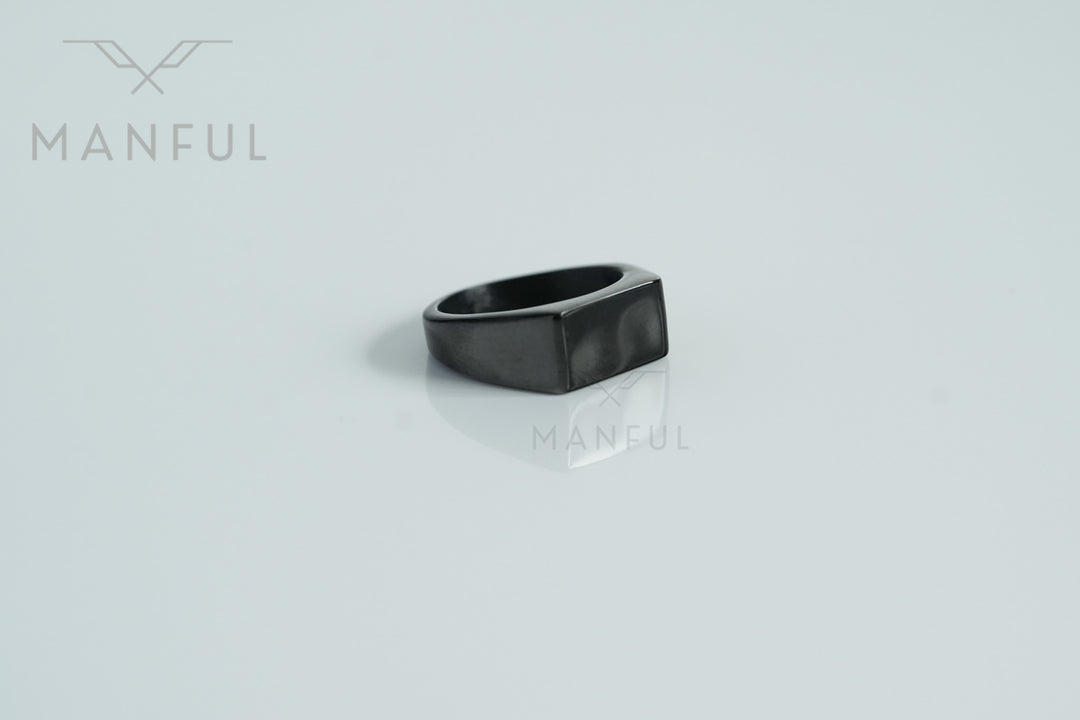 Rectangular Signet Ring Black, resting on a glossy white surface with a soft reflection