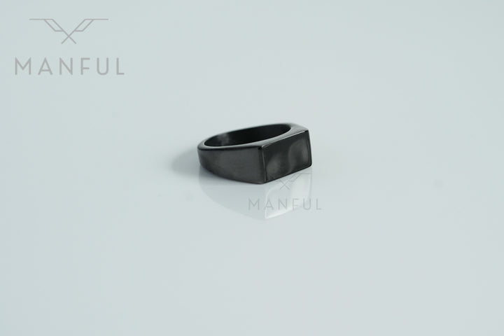 Rectangular Signet Ring Black, resting on a glossy white surface with a soft reflection