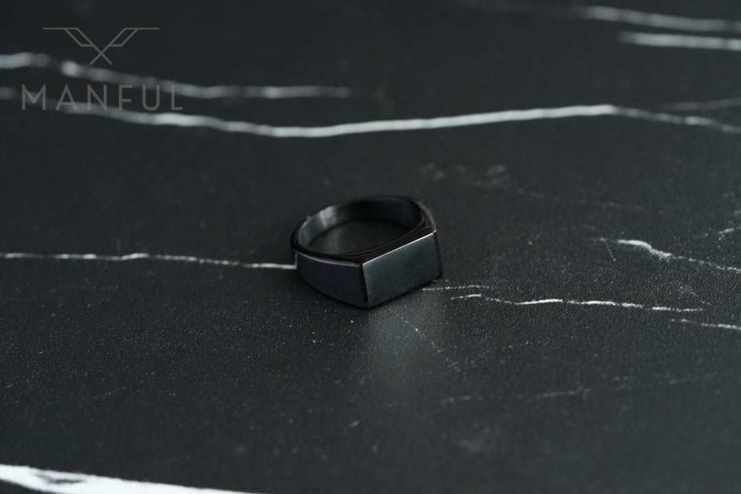 Rectangular Signet Ring Black, standing upright on a dark marble surface