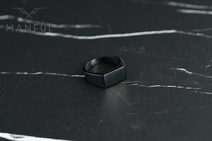 Rectangular Signet Ring Black, standing upright on a dark marble surface