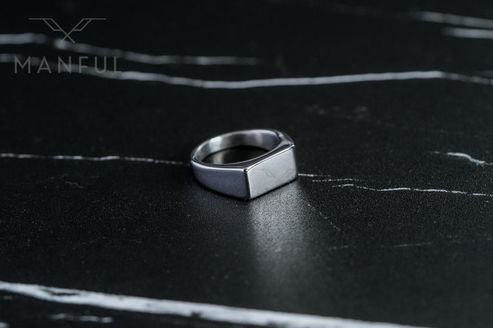 Rectangular Signet Ring Silver, resting on a dark marble surface with white veining