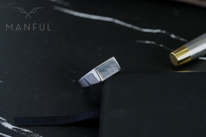 Rectangular Signet Ring Silver, angled on a black notebook with a gold-capped tube alongside