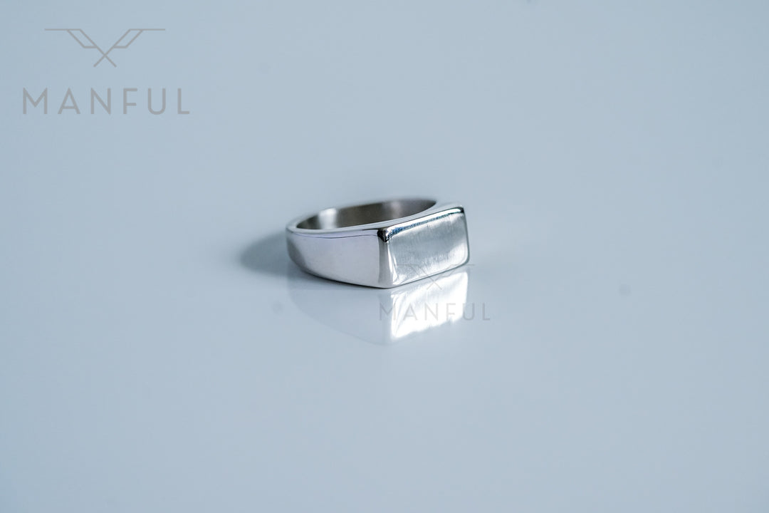 Rectangular Signet Ring Silver, resting on a pale grey surface with its reflection visible