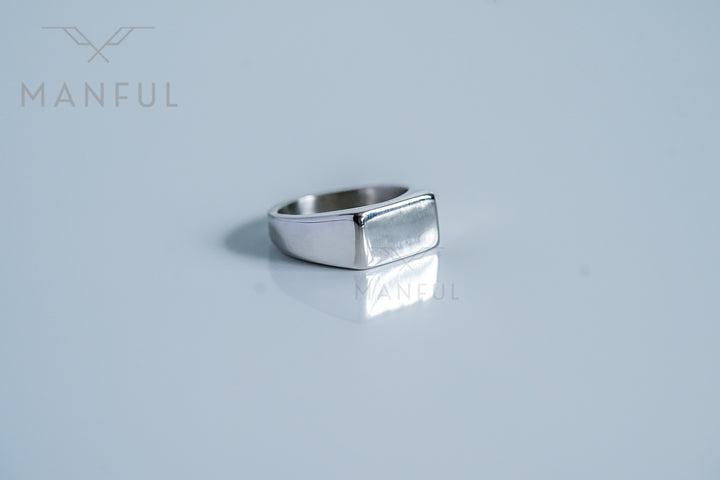 Rectangular Signet Ring Silver, resting on a pale grey surface with its reflection visible