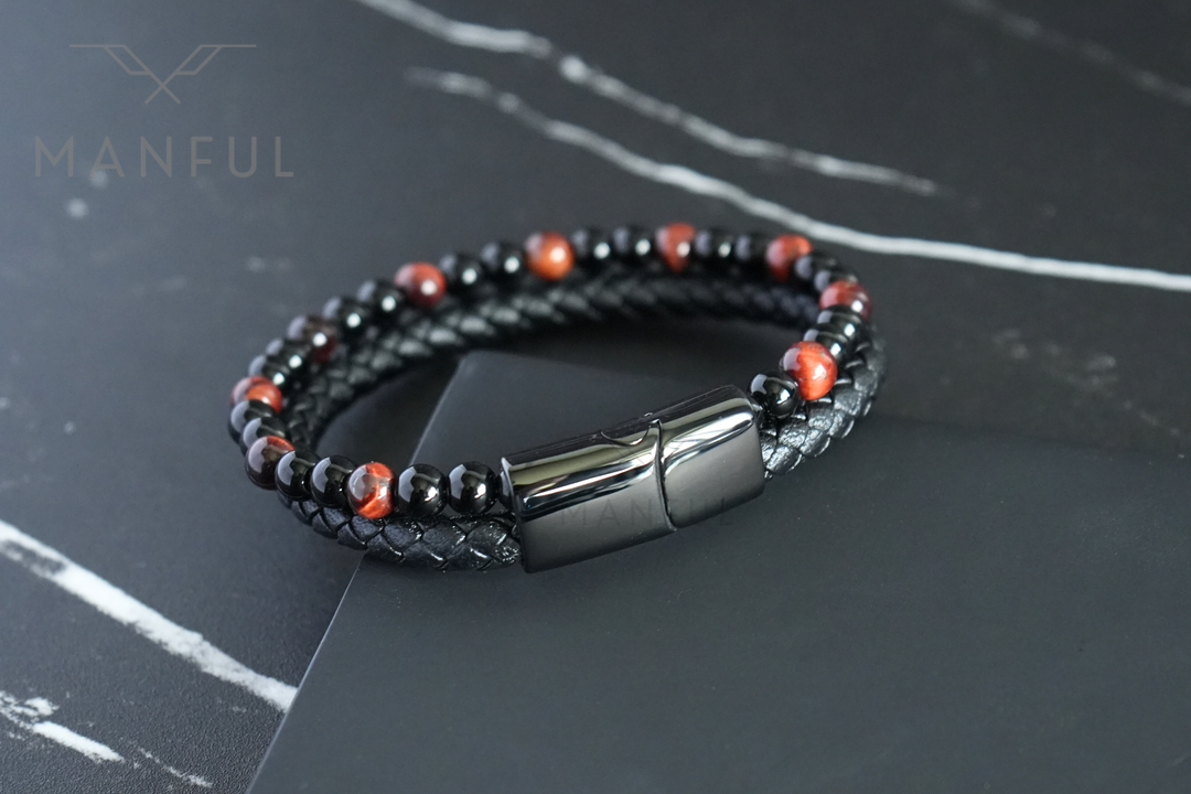 Red Tigers Eye Bead And Leather Bracelet, angled on a dark surface with the clasp facing forward