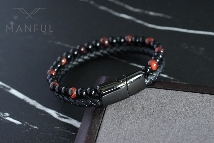 Red Tigers Eye Bead And Leather Bracelet, resting on a dark surface beside a wooden block prop