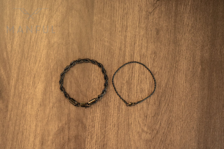 Rope Chain Bracelet Black, flat lay on wood beside a thinner silver-tone chain