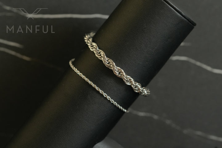 Rope Chain Bracelet Silver, wrapped around a leather roll beside a thinner chain on dark marble