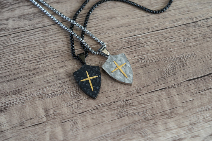 Shield Cross Pendant Black, close-up of the black pendant beside a silver version for comparison