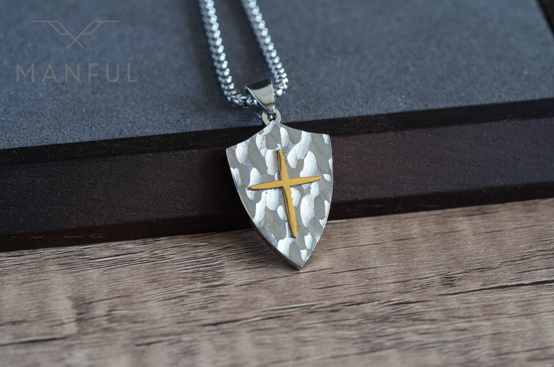 Shield Cross Pendant Silver, resting on a dark wooden block against a plank surface