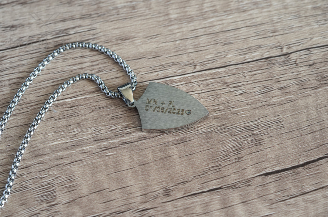 Shield Cross Pendant Silver, flipped over to show the engraved back on a wood surface