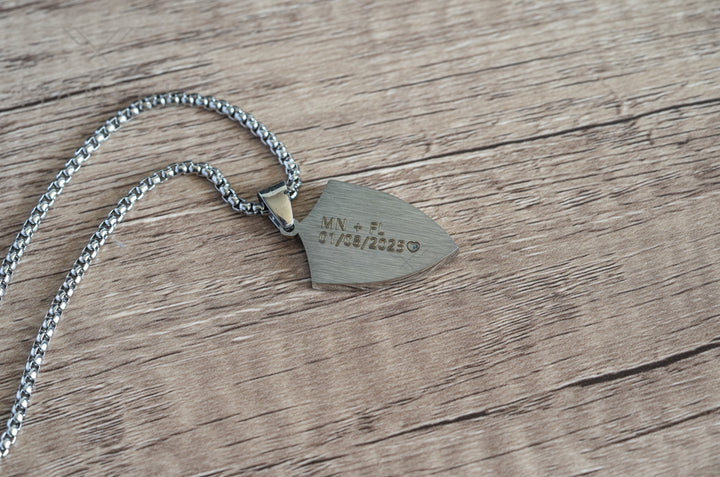 Shield Cross Pendant Silver, flipped over to show the engraved back on a wood surface