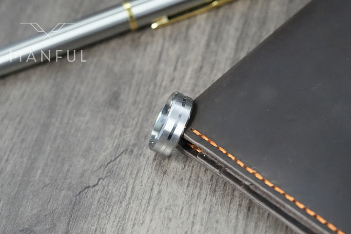 Silver Band, close-up resting against the spine of a brown leather notebook beside a pen