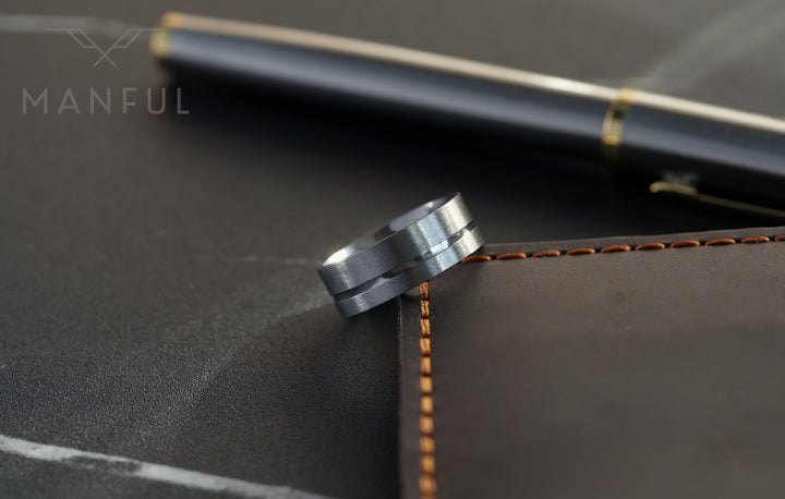 Off-balance Silver Band, propped against a leather notebook edge beside a pen