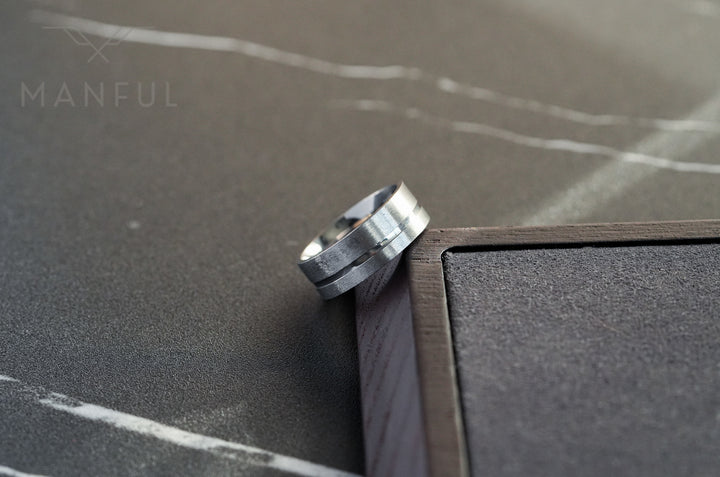 Off-balance Silver Band, propped against a wooden frame corner on a marble surface