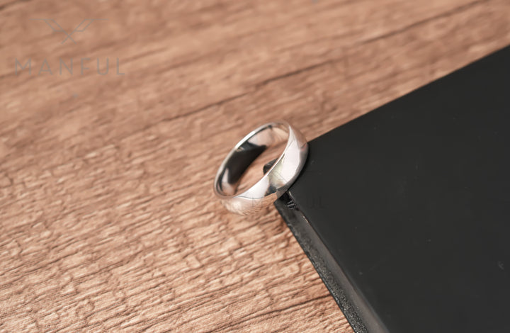 Simple 6mm 925 Silver Ring, leaning against the corner of a black book on a wood surface